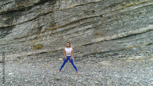 Woman is doing squats the bodyflex during breathing exercises on the rock background. Aerial beautiful footage view. photo