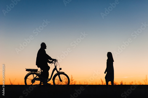 Male cyclist on the e-bike or electric bicycle on the sunset background. Silhouette of the man in profile. Active pension. Travel. Sport.