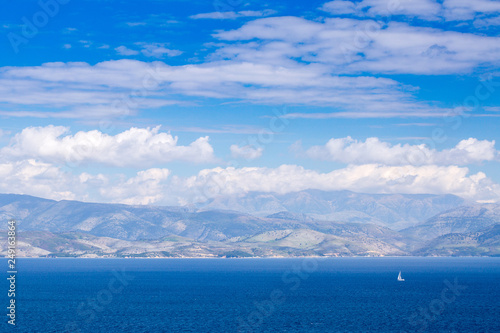Wonderful romantic summertime panoramic seascape. Sailing yacht with white sails in to the crystal clear azure sea against coastline slopes. © Sodel Vladyslav