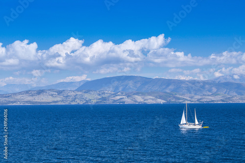 Wonderful romantic summertime panoramic seascape. Sailing yacht with white sails in to the crystal clear azure sea against coastline slopes.