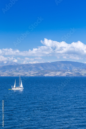 Wonderful romantic summertime seascape. Sailing yacht with white sails in to the crystal clear azure sea against coastline slopes.