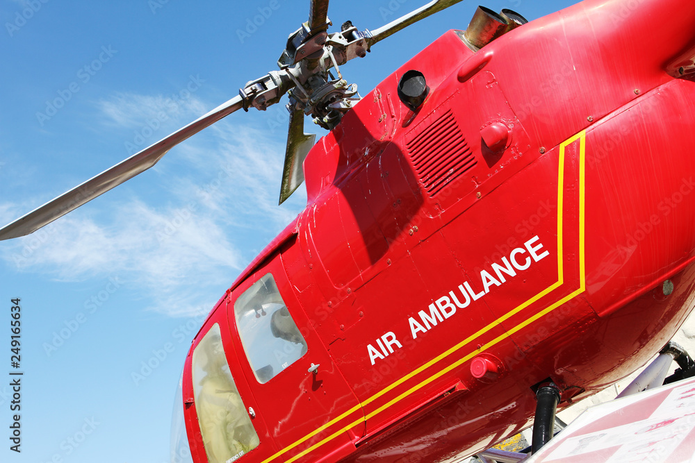 Naklejka premium Red helicopter of air ambulance isolated on blue sky background. Detail of the helicopter blades. Cornwall, UK