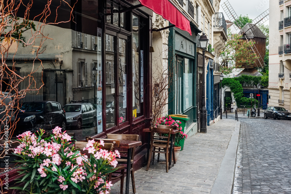 Fototapeta premium Przytulna ulica ze stolikami kawiarni i starego młyna w dzielnicy Montmartre w Paryżu, Francja