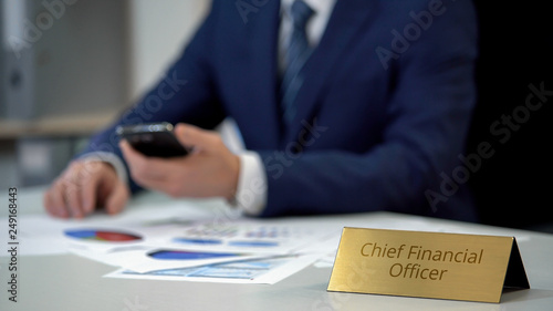 Chief financial officer checking data in annual report, using smartphone, work photo