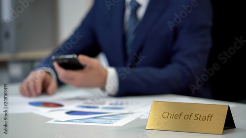 Fotografie Busy chief of staff using smartphone, analyzing corporate statistics diagrams