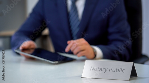 Schilderij op canvas Male notary public viewing files on tablet, checking documents for notarization