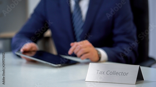 Photo Tax collector in suit using tablet computer for searching clients credit history