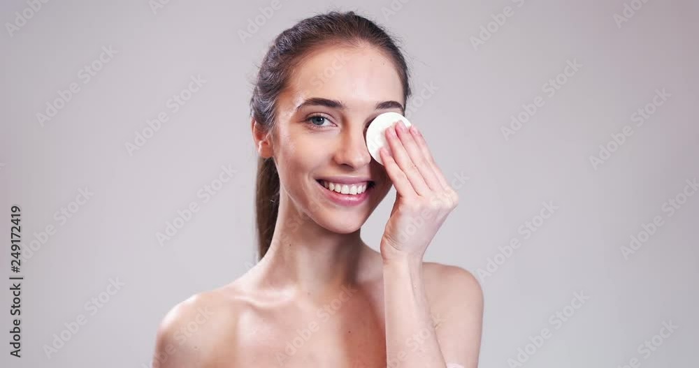 Beautiful girl hiding her eye with cotton swab pad, isolated on grey background Beautiful girl hiding her eye with cotton swab pad, isolated on grey background