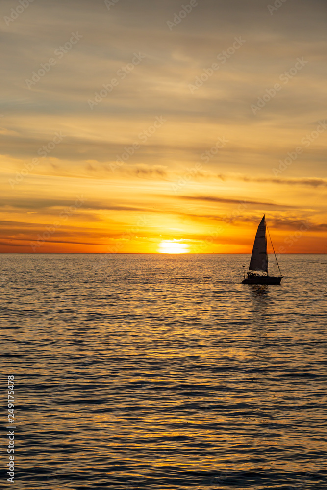 A silhouetted sailing boat on the ocean, against a sunset sky