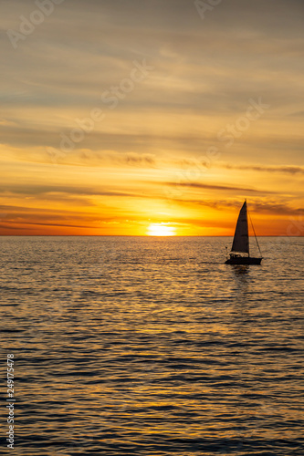 A silhouetted sailing boat on the ocean  against a sunset sky