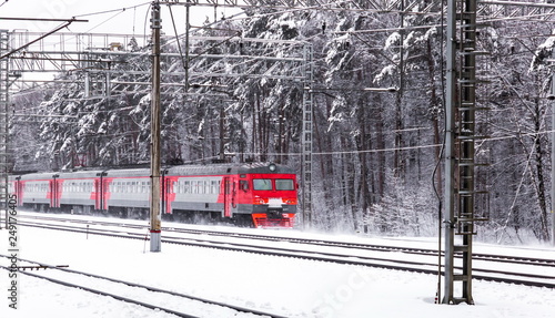 Red electric train moves through winter forest photo