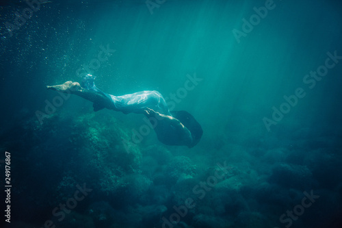 brunette girl in long blue dress dives underwater in the sea © Nikita