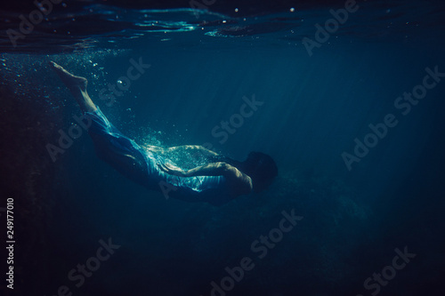 brunette girl in long blue dress dives underwater in the ocean © Nikita