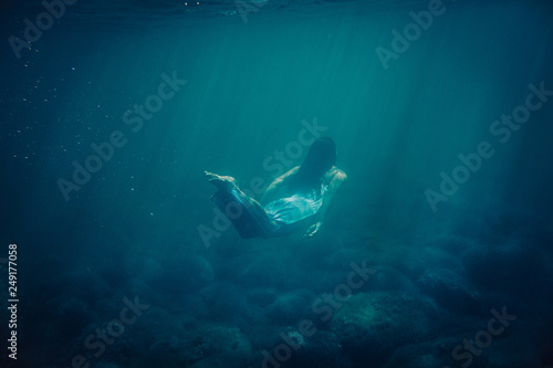 brunette girl in long blue dress floats underwater