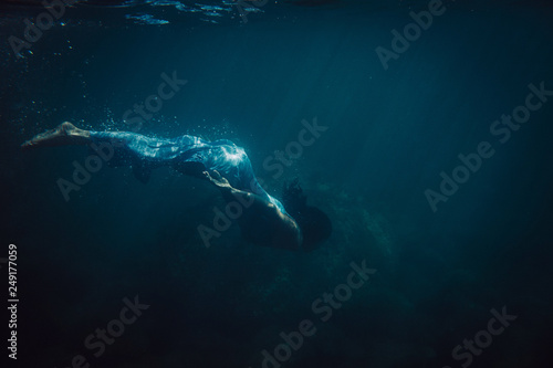 brunette girl in long blue dress swimming underwater photo