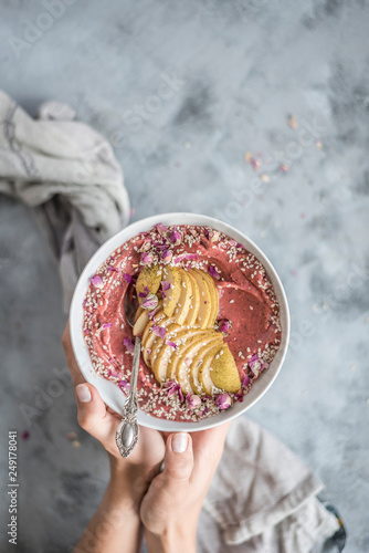 Hands Holding Pink Smoothie Bowl with Apples, Seeds & Flowers photo