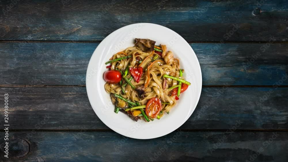 Rotating udon stir fry noodles with with seafood in a white plate on wooden background. Top view Rotating udon stir fry noodles with with seafood in a white plate on wooden background. Top view