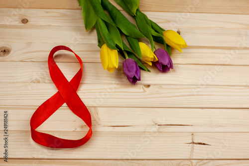 Bouquet of tulips on a light wooden background and figure 8 of satin ribbon gift for March 8