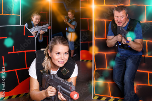 smiling girl with laser pistol playing laser tag with friends