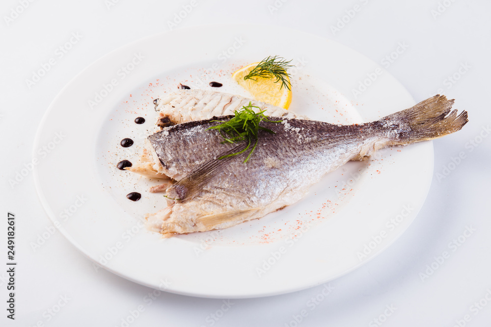 grilled dorada in salt with lemon slice on a white plate on a light background (close)