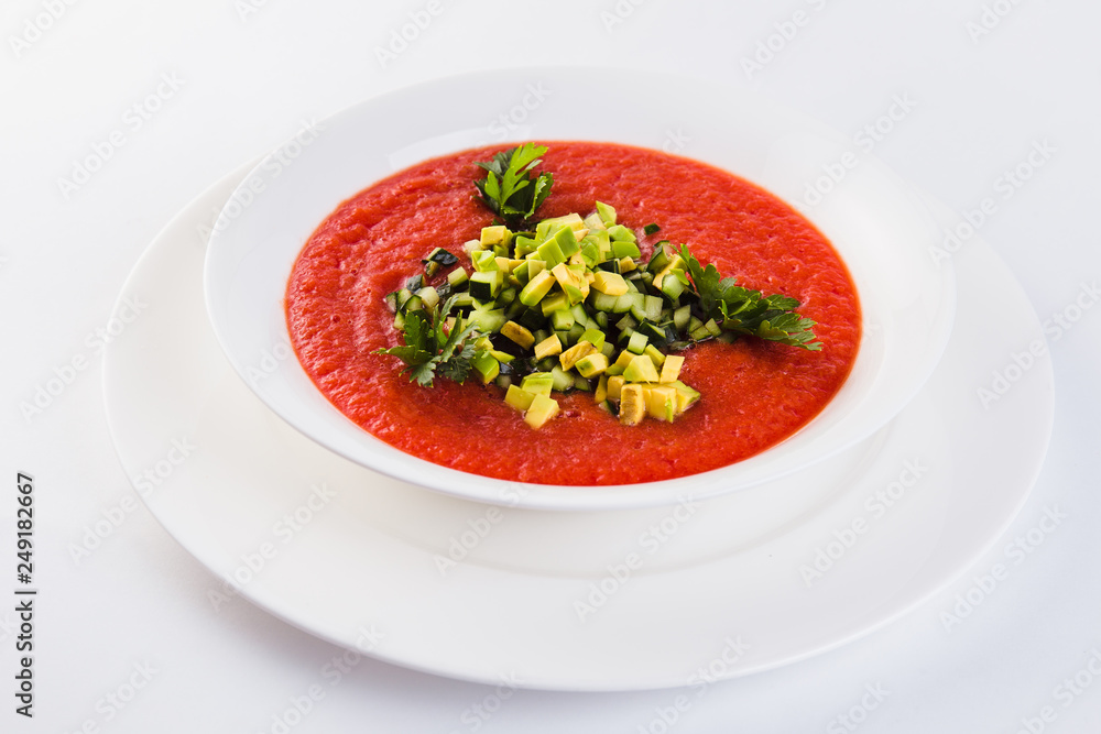 Spanish soup gazpacho with avocado and cucumber on a white plate on a light background (close) Spanish soup gazpacho with avocado and cucumber on a white plate on a light background (close)
