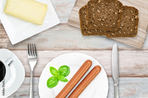 Top view of simple and energetic brakfast ( coffee, butter, dark bread, sausages) in rustic style on a wooden vintage table 