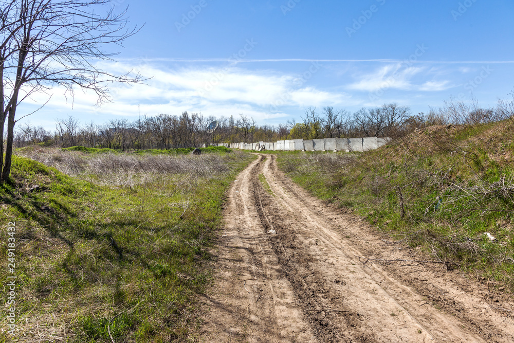 Unpaved country road without asphalt. A rough nameless dirt road on the outskirts of Ukraine. Stony roads in the steppe. Dirty road without pavement runs into perspective into the distance