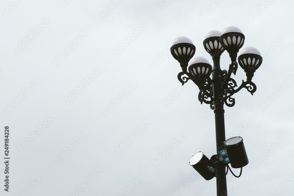 Streetlight with five spherical lamp on black vintage pillar on background of cloudy sky. Streetlight in overcast weather with copy space. Street lamps close-up. Two spotlights on pole.