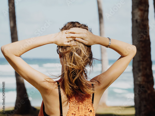 young girl on vacation on the shore of the blue ocean. strong wind blows on hair. back view. photo