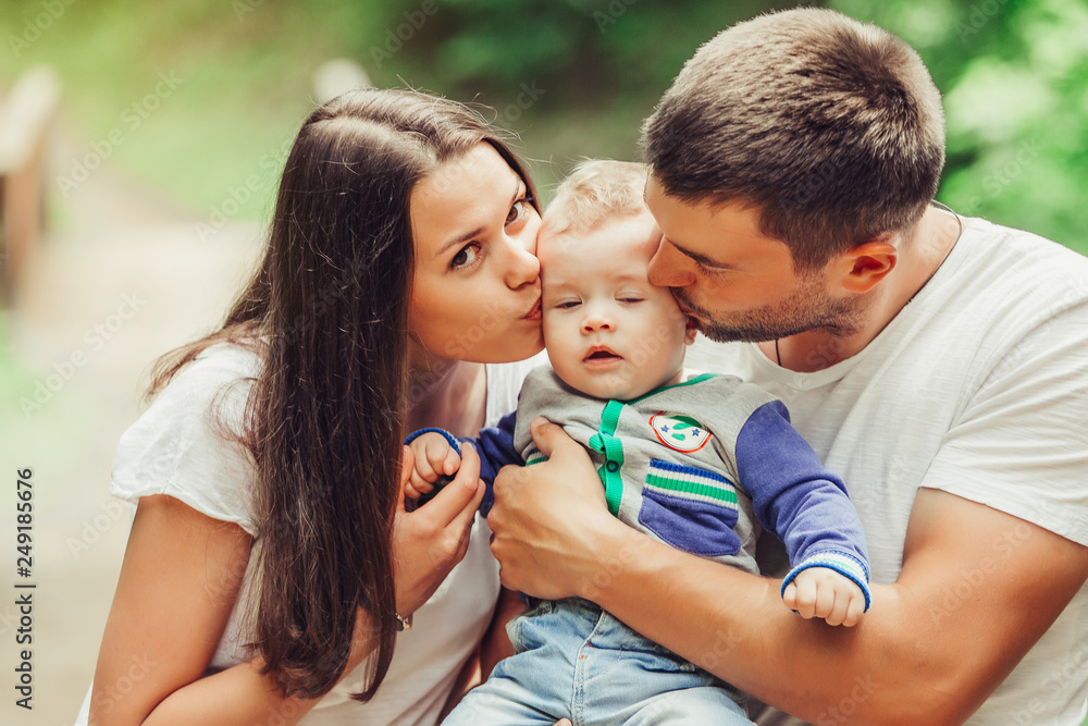 Happy loving young family with infant baby walking together in green summer park hugging each other. Family, togetherness, childhood concept Happy loving young family with infant baby walking together in green summer park hugging each other. Family, togetherness, childhood concept