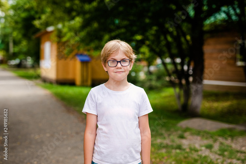 Blonde smiling boy with strabismus wearing glasses with special lens in warm park