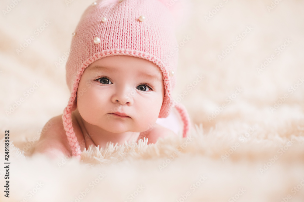 Cute baby girl wearing knitted hat lying in bed closeup. Looking at camera. Childhood. - obrazy, fototapety, plakaty 