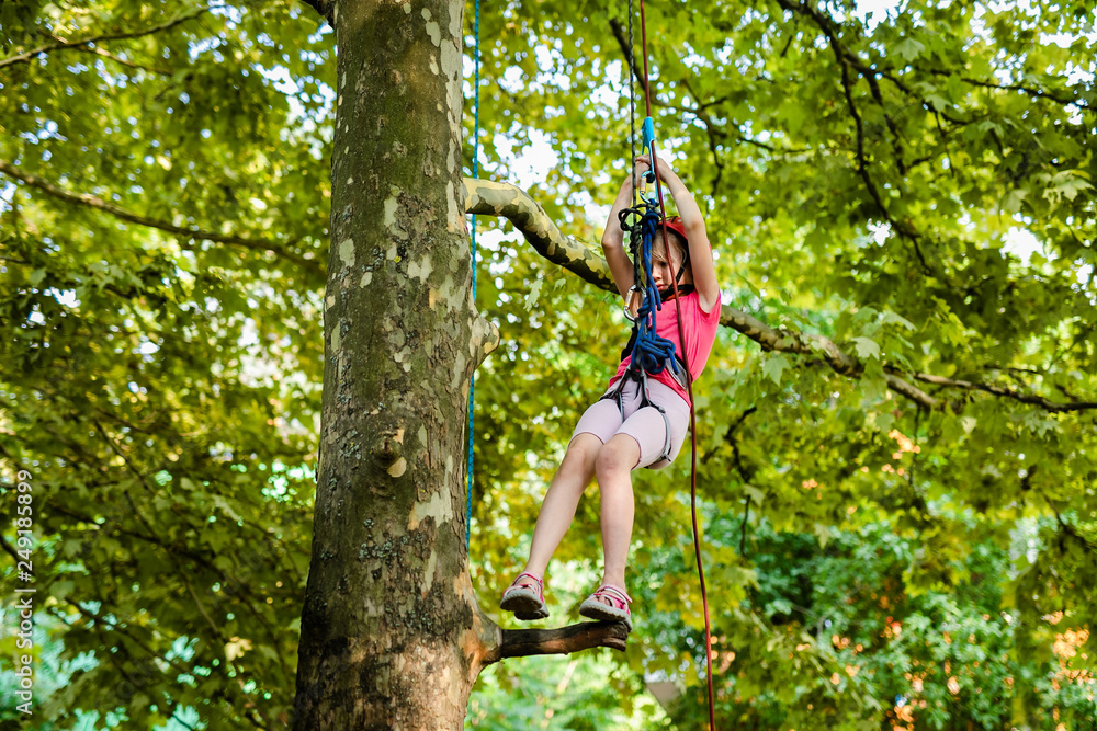 Blonde teenager girl in red helmet and pink clothes climbing on the tree with ropes Blonde teenager girl in red helmet and pink clothes climbing on the tree with ropes