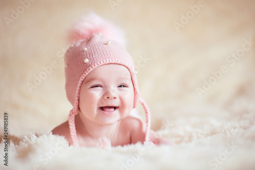 Happy baby girl wearing stylish knitted hat lying in bed close up. Childhood. photo