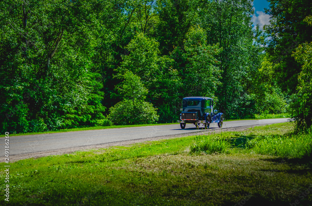 Blue antique car on a winding road through trees