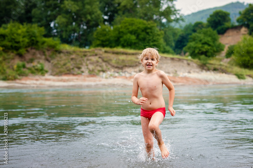 Blonde smiling boy with strabismus playing on the river
