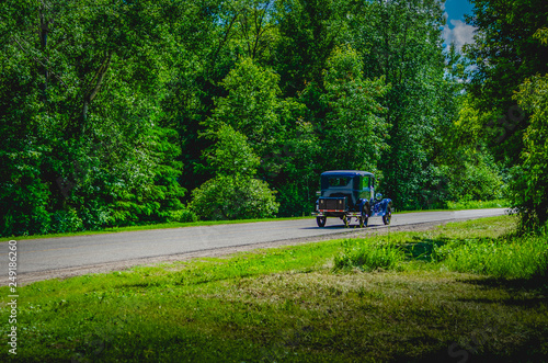 Blue antique car on a winding road through trees