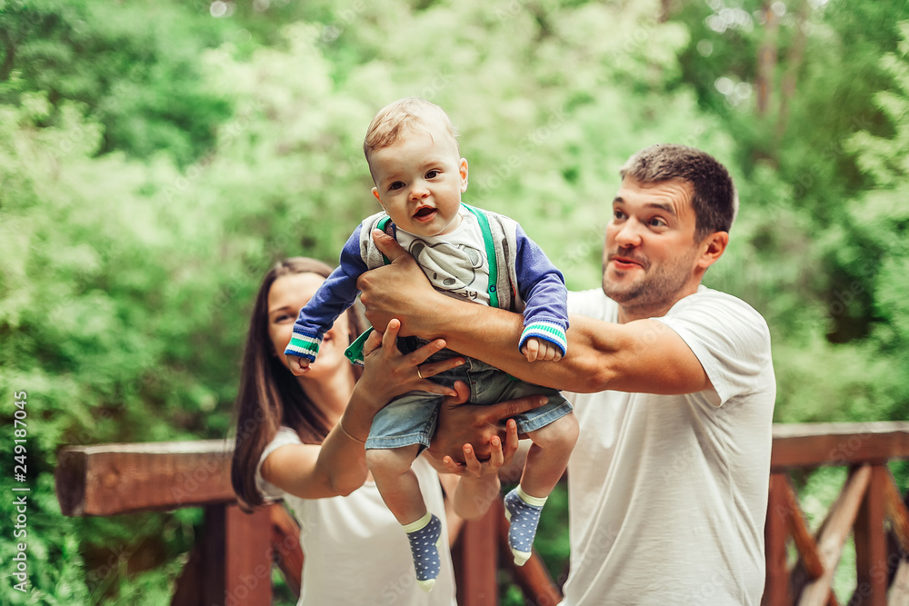 Happy loving young family with infant baby walking together in green summer park hugging each other. Family, togetherness, childhood concept Happy loving young family with infant baby walking together in green summer park hugging each other. Family, togetherness, childhood concept