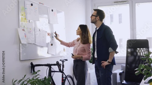 Two colleagues writing on whiteboard while brainstorming in startup hub office