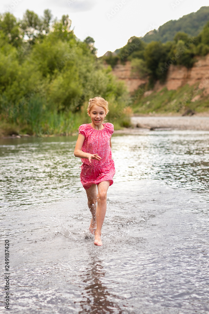 Blonde smiling girl in the pink dress playing on the side of mountain river Blonde smiling girl in the pink dress playing on the side of mountain river