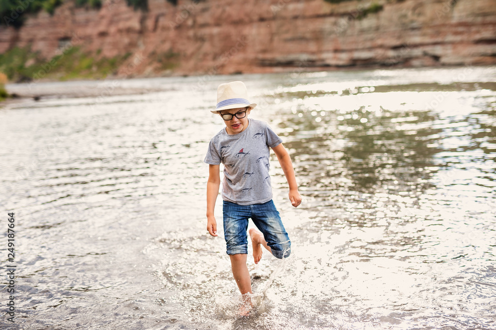 Blonde smiling boy with strabismus playing on the river