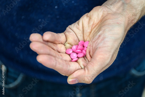 Close-up of man holding pink pills in his hand.Concept of an old man trying to get his medicine.
