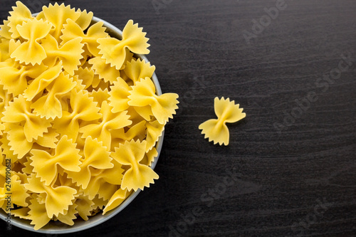 Top view of black background with italian raw farfalle or pasta in bowl with copy space