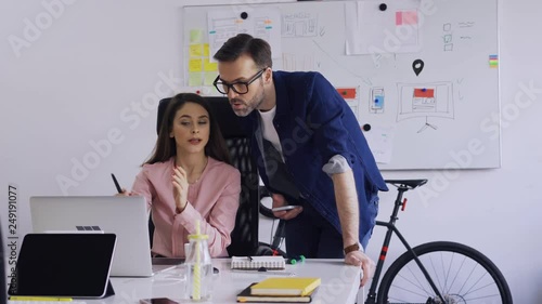 Two coworkers discussing while looking at laptop in small office