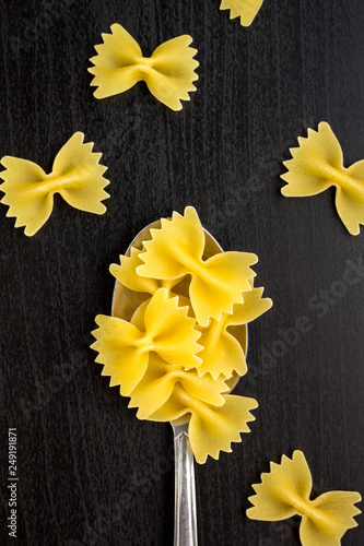 italian raw farfalle pasta dry on a metallic spoon and an black table