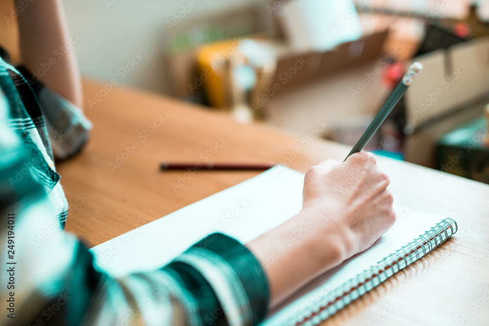 Close up of woman's hands writing in spiral notepad placed on wooden desktop Close up of woman's hands writing in spiral notepad placed on wooden desktop