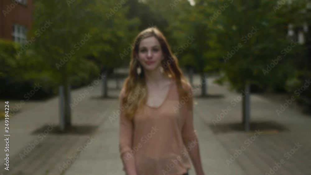 Young Woman Walks Toward Camera Through City Park, She Stops And Pulls Her Hair Back And Smiles For Camera Young Woman Walks Toward Camera Through City Park, She Stops And Pulls Her Hair Back And Smiles For Camera