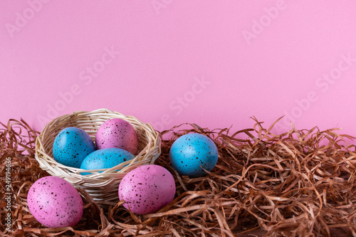 Six pink and blue Easter eggs in a basket on pink background. Easter celebratory wallpaper with copy space.