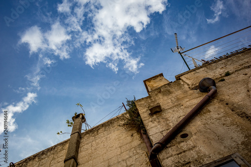 Street view from the historic center of Altamura, Italy, Puglia region, the edge of residential building with pipes, chimney and antennae as seen from below, scenery summer day with puffy white clouds