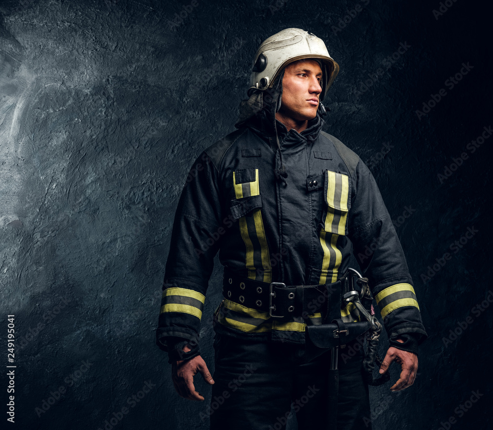 Manly firefighter in helmet looks sideways in studio on black background